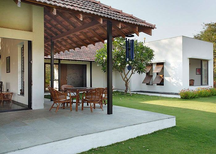 Shaded villa patio with wicker outdoor furniture, terracotta tile roof, and a lush green lawn.