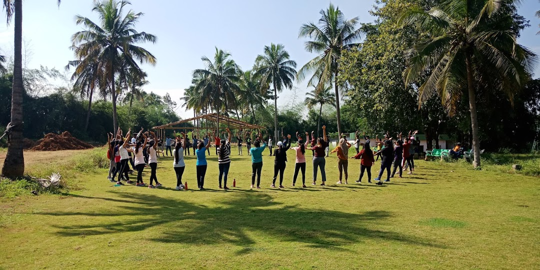Corporate team-building activity at a spacious outdoor farmhouse resort surrounded by palm trees and greenery.