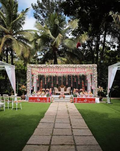 **Alt text:** Modern luxury farmhouse wedding venue with floral stage decoration, green lawn, and tropical trees.